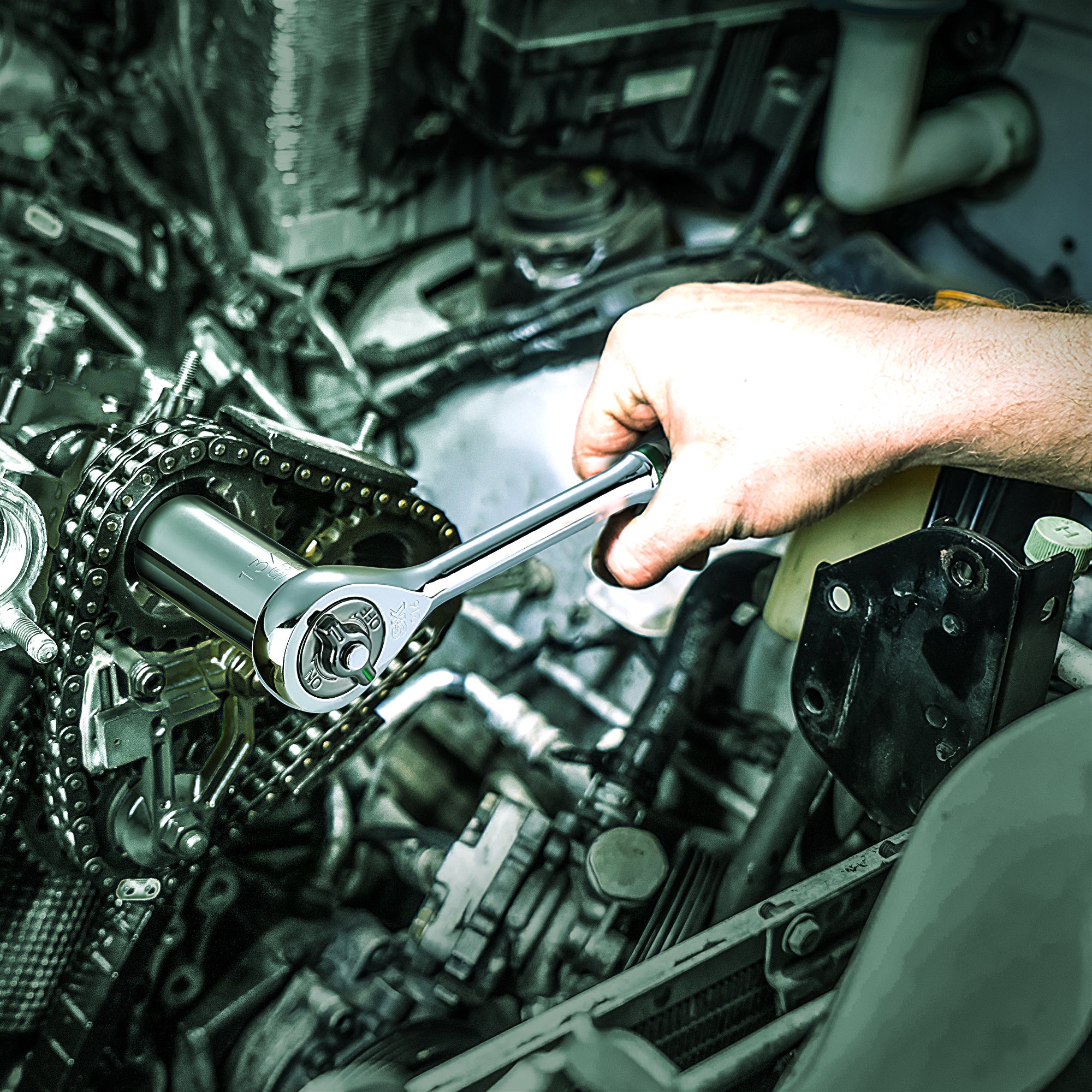 A hand using a ratchet wrench on an engine's timing chain in a mechanical setting.